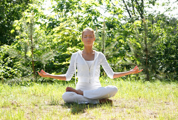 A young and attractive woman is meditating in a forest