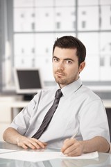 Fototapeta premium Young businessman sitting at desk writing notes