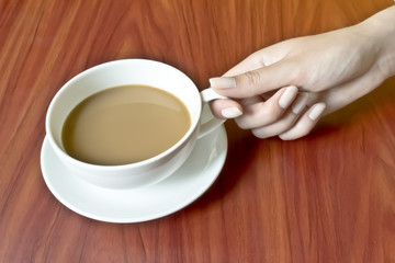 female hand with manicure holding a cup of hot coffee