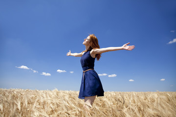 Redhead girl at wheat field in summer day.