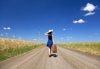 Lonely girl with suitcase at country road.