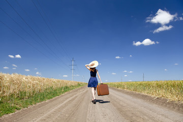 Lonely girl with suitcase at country road.