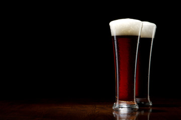 two Beer into glass on a black and wooden table