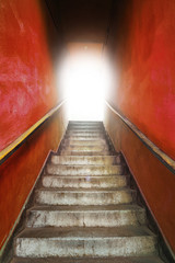 Old grungy stairs with handrails on red wall with light on top