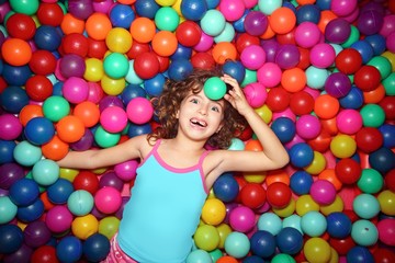 Fototapeta na wymiar little girl playing lying in colorful balls park playground