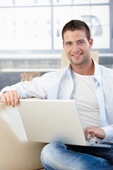 Handsome man with laptop smiling on sofa