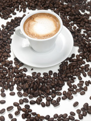 Taza de café con leche y espuma juntoa granos de café esparcidos sobre un fondo blanco. Vista superior y de cerca