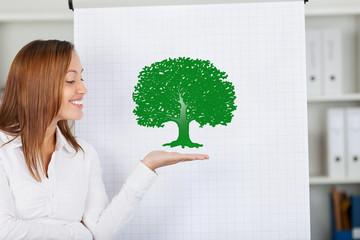 frau im büro zeigt grünen baum