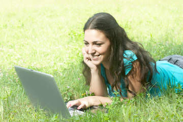 Young woman with laptop lying on grass