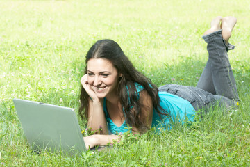 cute young female lying on the grass in the park using a laptop