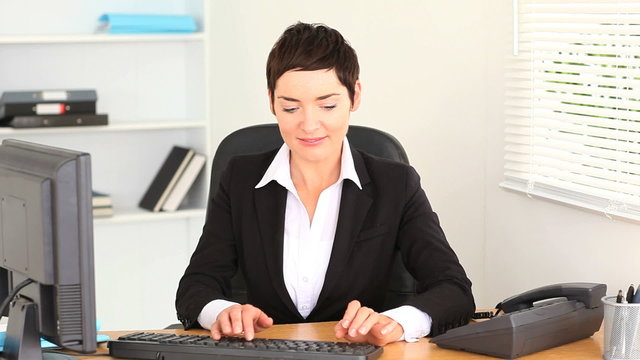 Brunette woman typing on a laptop and answering the phone