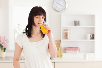Fototapeta premium Gorgeous brunette drinking a glass of orange juice while standin