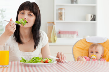 Attractive brunette woman eating a salad next to her baby while