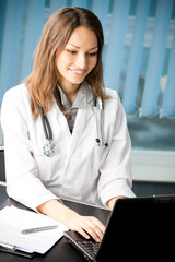 Happy smiling female doctor or nurse working with laptop