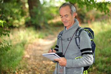 sixty years old man taking notes on a forest trail