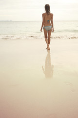 Young woman standing on wet perfect sand and going to swim in a sea