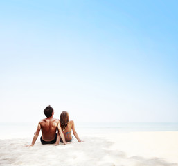 Fototapeta premium Young couple sitting on white sand by sea and enjoying each other