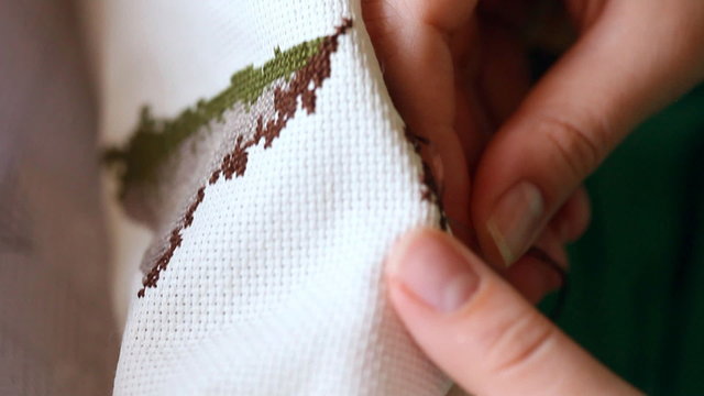 Woman hands doing cross-stitch. A close up of embroidery.