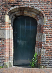 Green wooden door in deformed brick wall