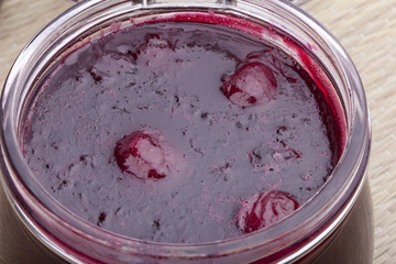 studio-shot of homemade cherry jam in a glass jar.