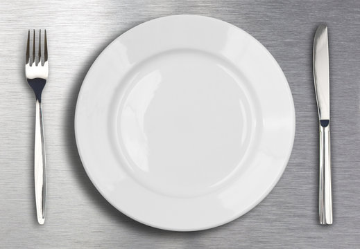 Knife, white plate and fork on metal background