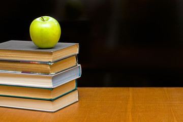 Green apple and  books on the desk.