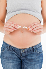 Pregnant woman holding a broken cigarette while standing