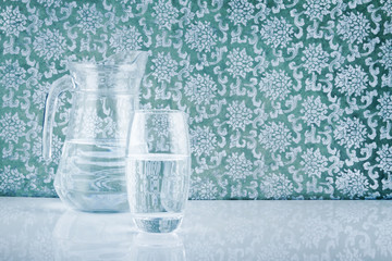 glass and jug filled with fresh water on patterned backdrop