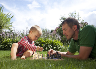 Child and father playing chess in the garden