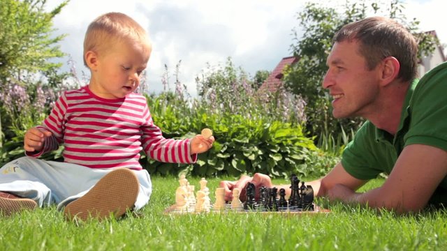 Father and baby playing chess on the grass