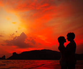 Young couple standing on the sand by sea on red dramatic sunset background