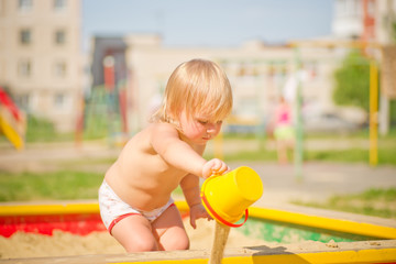 Adorable baby play with toy pail stay on sandbox  on playground.