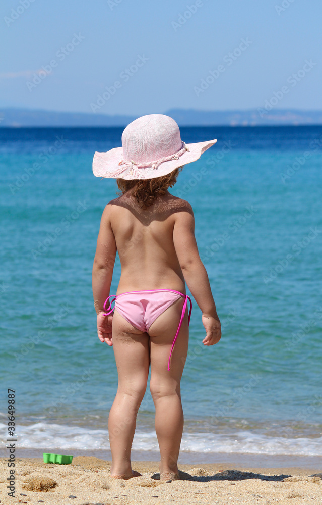 Wall mural little girl with straw hat looking at sea