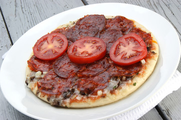 Pizza mit Paprikasalami auf einem weißen Teller
