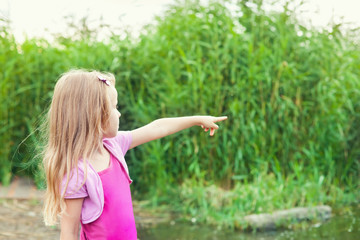 Obraz premium blonde little girl shows forefingers aside near river with canes