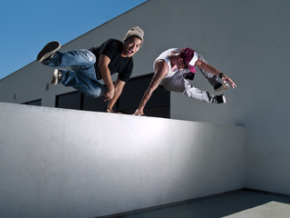 two male parkour free runners jumping over a wall