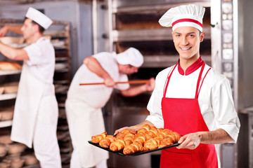 Male baker holding freshly baked croissants in bakery - obrazy, fototapety, plakaty