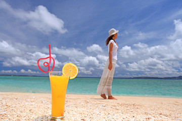 砂浜に置かれたソフトドリンクと海を眺める女性
