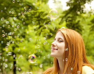 Redhead girl in the park under soap bubble rain.