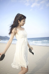 Fototapeta na wymiar サンダルを手に持って砂浜を歩く女性