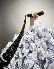 Hand with phone reaches out from heap of papers