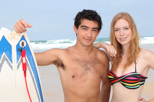 couple of teenagers posing with surfboard in front of the sea