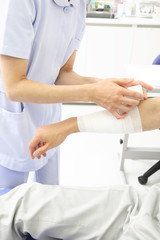 Obraz premium 患者の腕に包帯を巻く看護師の手元
