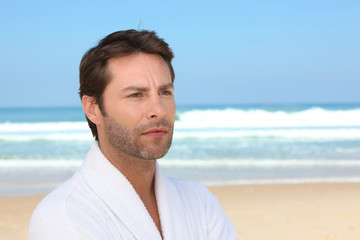 Fototapeta premium Distracted man standing on the beach in a bathrobe