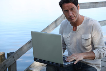 Man using a laptop computer by the water
