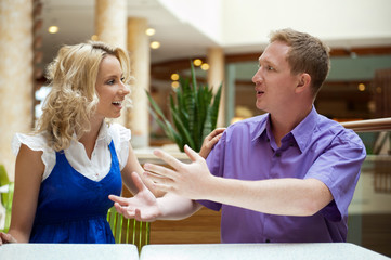 Young debating or talking couple inside mall sitting near the ta