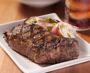 grilled steak with potatoes and cola in background.