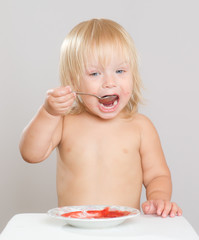 Adorable toddler girl eat strawberry jam with spoon from plate