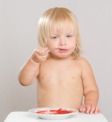 Adorable toddler girl eat strawberry jam with spoon from plate