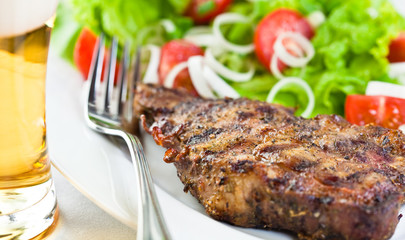 Grilled pork steak with salad and a glass of beer